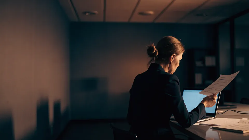 A finance director reviewing an invoice beside a laptop in a quiet office